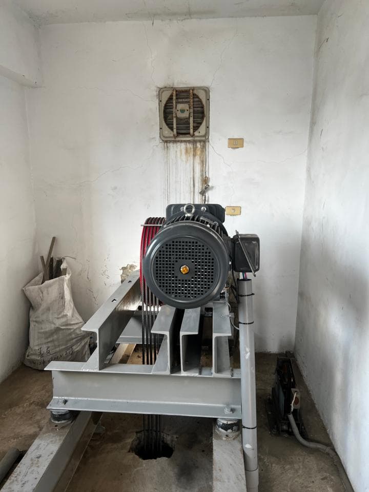 1) 照片顯示一個電梯機房,牆上有一個通風口,機房內有一個電梯的馬達