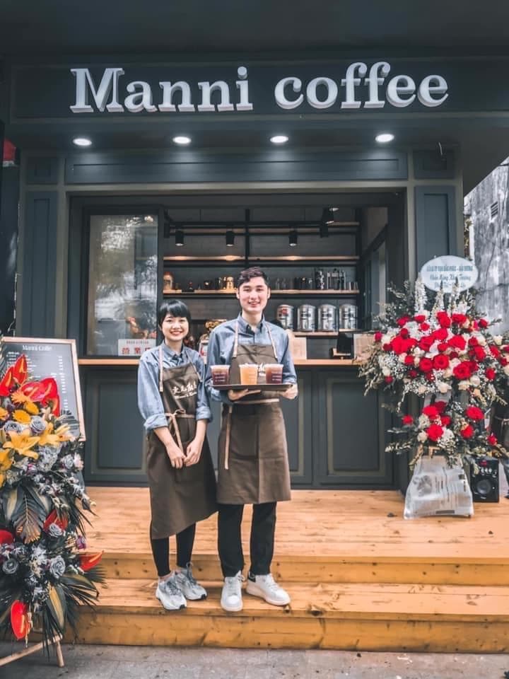 這張照片是兩位身穿圍裙的咖啡店員站在一家名為 Manni coffee 的咖啡店門口。