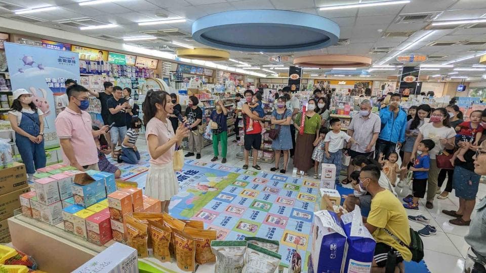 這張照片是一個超市的活動現場,中間放著一個巨大的產品展示臺,上面擺滿了各種商品,周圍圍繞著許多人,他們都在仔細地觀看和了解產品。