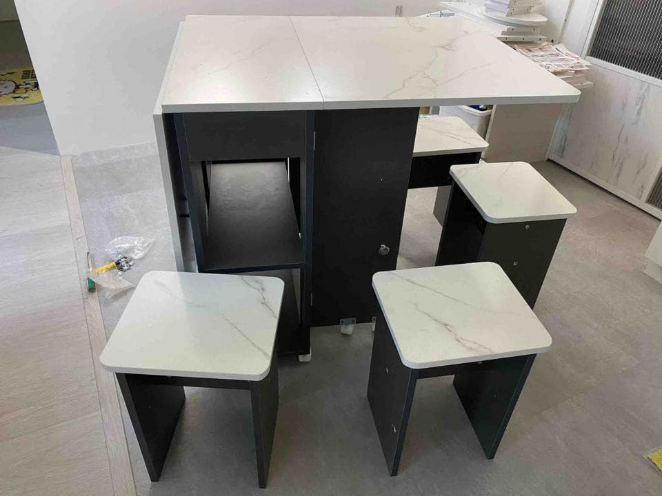 這張照片是一張可摺疊的餐桌,帶有四把椅子。桌子和椅子都是以白色和黑色為主色調,桌面和椅子座面都採用大理石紋路設計,看起來非常時尚簡潔。