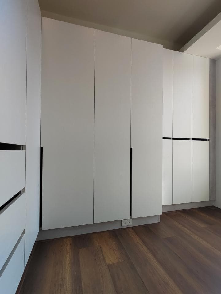 這張照片是一間房間,牆壁上有很多白色的櫃子,地面是深棕色的木地板。