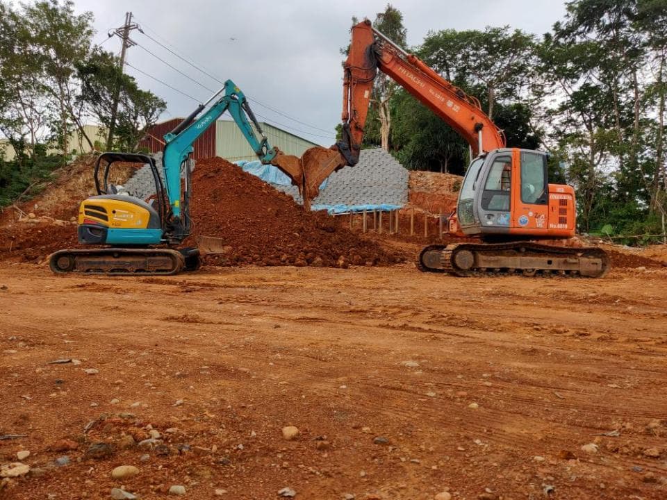 1) 照片顯示兩台挖掘機停放在紅土地上,背景是一片樹林