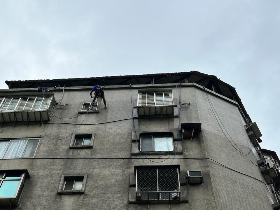 1. 這張照片顯示一棟建築物的外牆,一個工人在建築物外牆上進行清潔作業,他的工具和安全繩索都可見