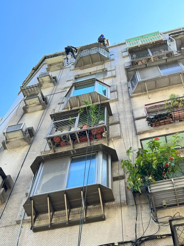 1) 這張照片顯示一棟高樓的側面,有工人正在進行高空作業,可以看到他們懸掛在繩索上,並使用安全裝備進行作業