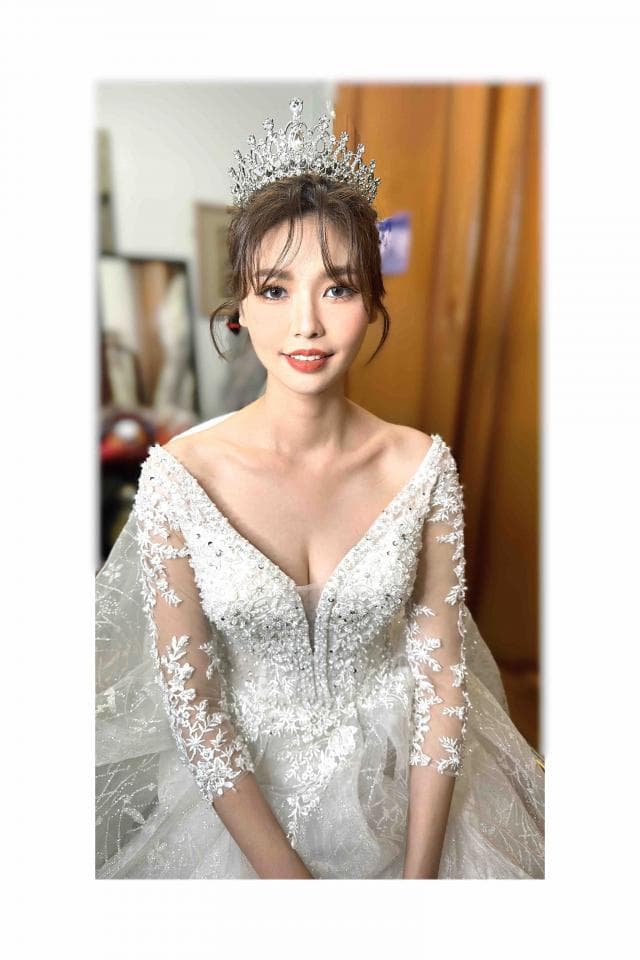 這張婚紗照是一位頭戴閃亮皇冠的新娘,她身穿著蕾絲花邊婚紗,露出迷人的微笑。