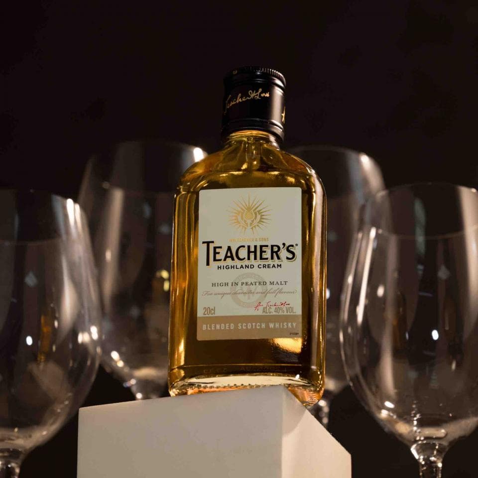 這張「教師高地奶油蘇格蘭威士忌」的照片是,一瓶教師高地奶油蘇格蘭威士忌放在幾杯酒杯上,背景是黑色的。