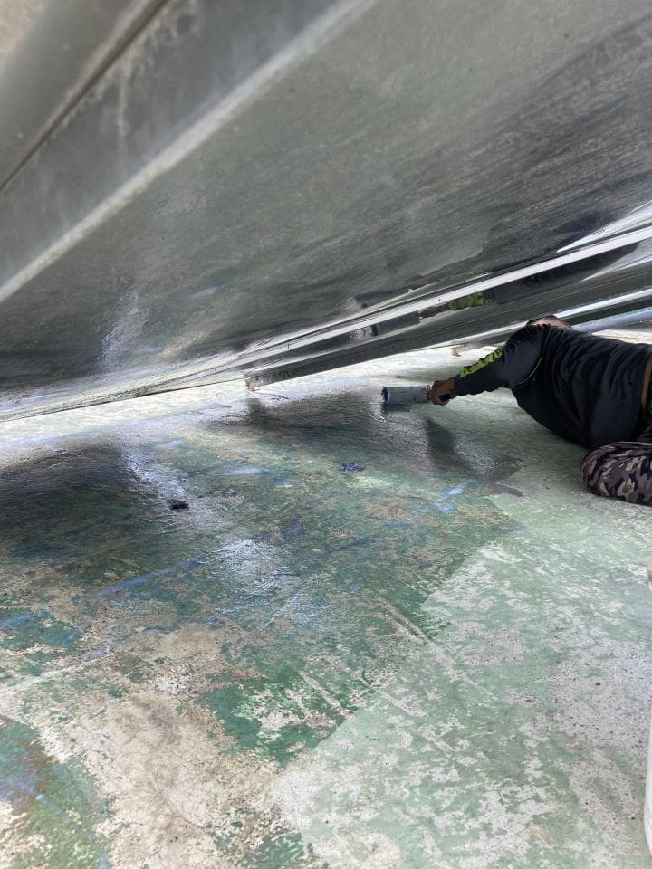 1) 照片顯示一個灰色的船體底下,一個人正在清洗船體底部,地面上是混凝土,顏色是灰色、白色和綠色