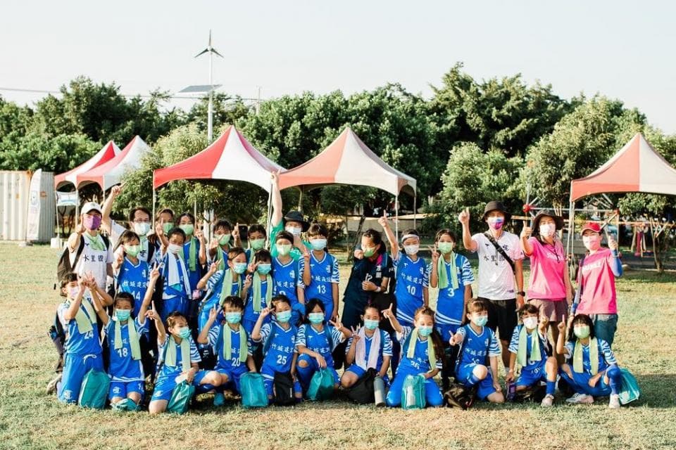 這張「一群穿著藍色運動服的孩童,在草地上玩耍」的照片是,他們戴著口罩,有的在玩遊戲,有的在聊天,看起來很開心。