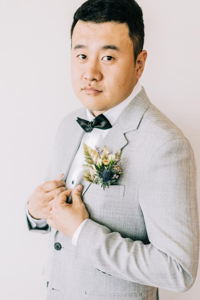 這張照片是一個穿著灰色西裝的男人,他正在整理胸前的花。