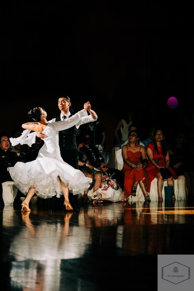 這張「舞蹈」的照片是一個穿著白色禮服的女性,和一個穿著黑色西裝的男性正在跳華爾滋,背景是其他觀眾。