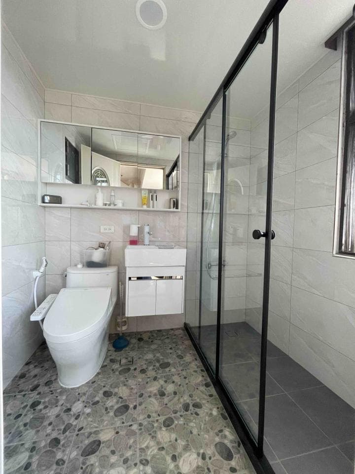 1) 照片顯示一個現代浴室,配有白色馬桶、白色洗手台、鏡子、以及黑色框玻璃淋浴間