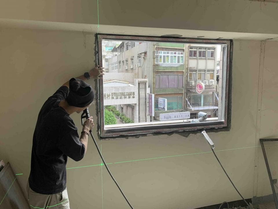 這張照片是一個工人正在用激光水平儀裝窗戶。