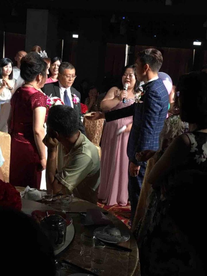 這張婚禮的照片是一個婚禮上的祝酒儀式,其中一對新人,一個穿著西裝的男子和一個穿著粉紅色禮服的女子正在被大家祝福,他們周圍圍繞著許多親朋好友,場面十分溫馨。