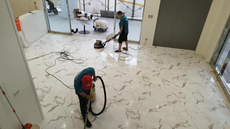 這張照片是一間正在清潔的大理石地板的房間,地板上有兩個人用機器清潔,機器後面留下乾淨的地板。