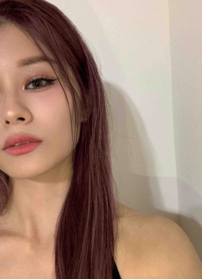 這張照片是一個年輕女性的近照,她的頭髮是深紫色,眼妝很淡,嘴唇是裸色,看起來非常自然。