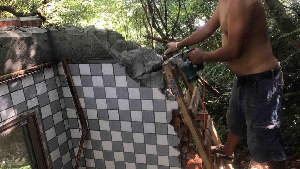 1) 照片中有一位男子站在梯子上,他正在使用電鑽破壞一堵以黑白瓷磚砌成的牆