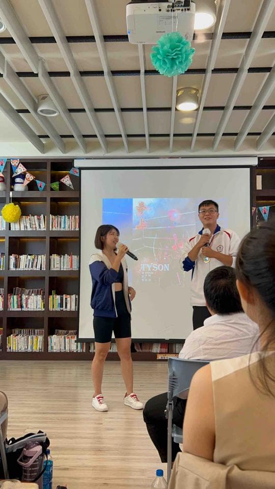 這張「圖書館」的照片是兩個年輕人在臺上演講,一位女生,一位男生,他們都在臺上拿著麥克風,臺下有觀眾在聽他們演講。