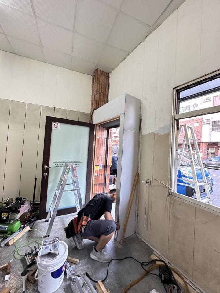 1) 照片顯示一個正在裝修的房間,房間裡有一位工人正在用工具修補牆壁,牆壁上有梯子、工具和油漆