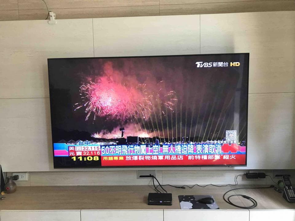這張照片是一台掛在牆上的電視,電視正在播放電視新聞,畫面上是煙火的畫面,時間顯示為晚上11點08分。
