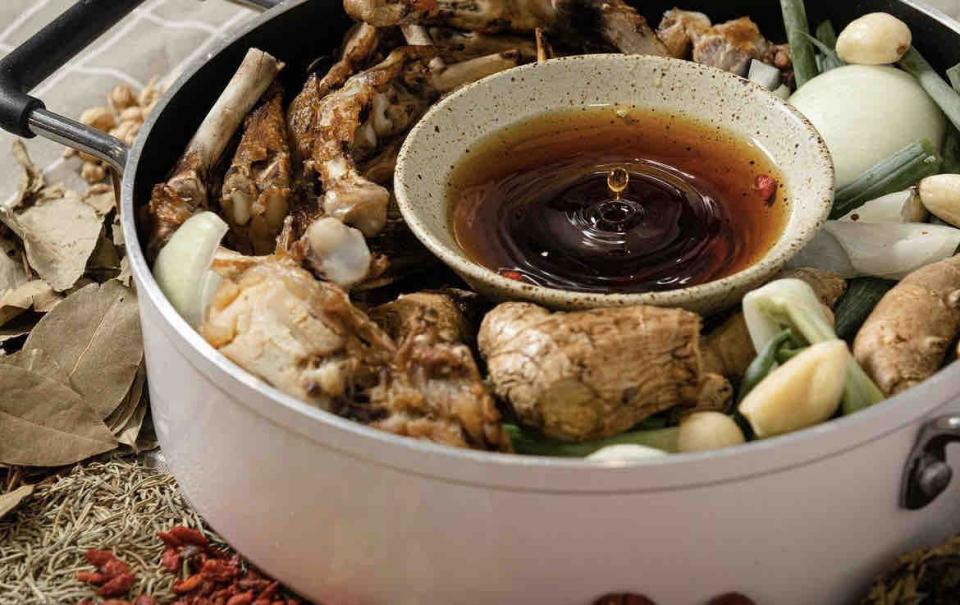 這張「燉湯」的照片是一個白鍋,裡面放了雞骨、薑、蔥、蒜等食材,以及一個裝滿醬油的小碗。