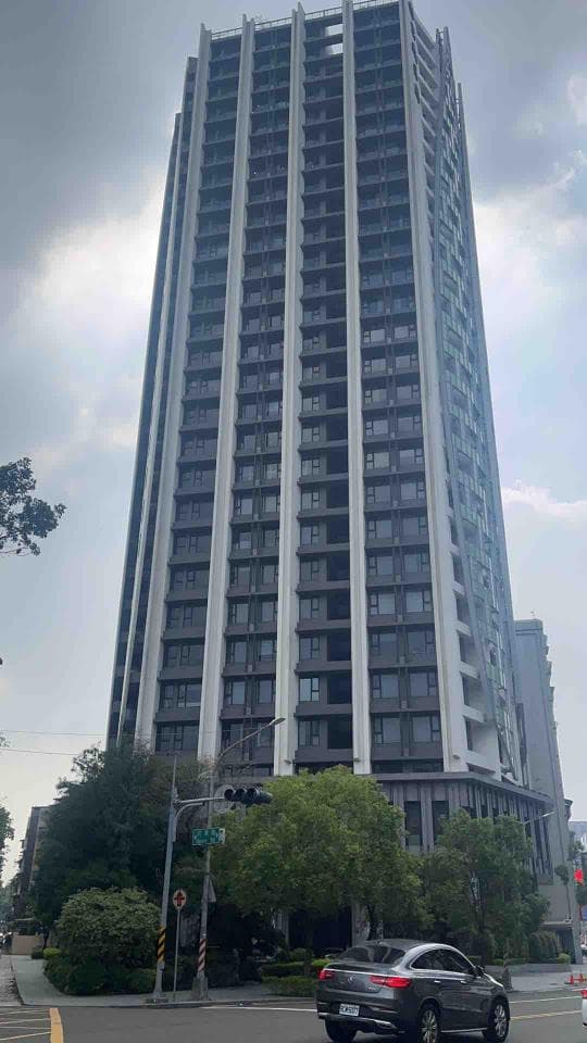 這張照片是一棟高聳的現代化建築,外牆以灰色與白色相間,呈現出簡潔俐落的風格。建築的窗戶設計整齊劃一,陽台則隱藏在建築外牆之中,整體外觀展現出現代化的風格。