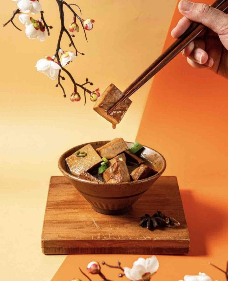 這張「豆腐」的照片是一碗滷豆腐,用筷子夾起一塊豆腐,擺放在木質託盤上。