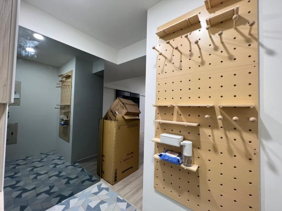 這張「牆上掛著一個帶有許多洞的木板,上面掛著各種東西,例如架子、鉤子、置物盒等等。」的照片是。