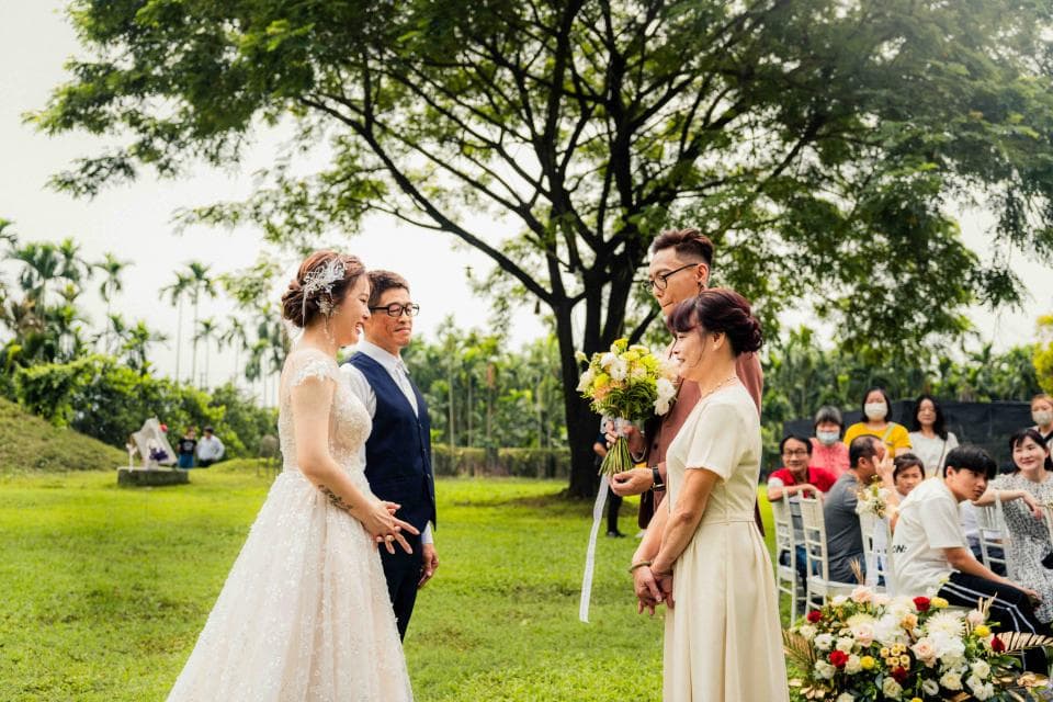 這張婚禮的照片是一對新人正在交換誓言,女方穿著白色婚紗,男方則穿著西裝,後面有親朋好友觀禮。