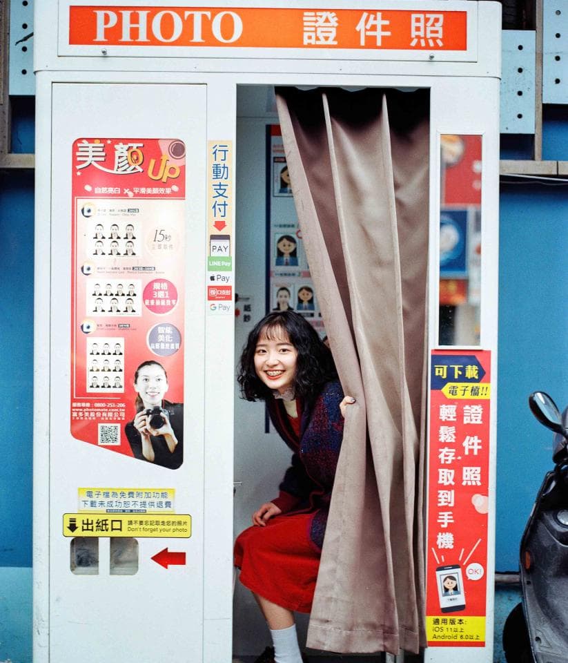 這張「照相亭」的照片是一個年輕女子在照相亭裡,她正要拍照。