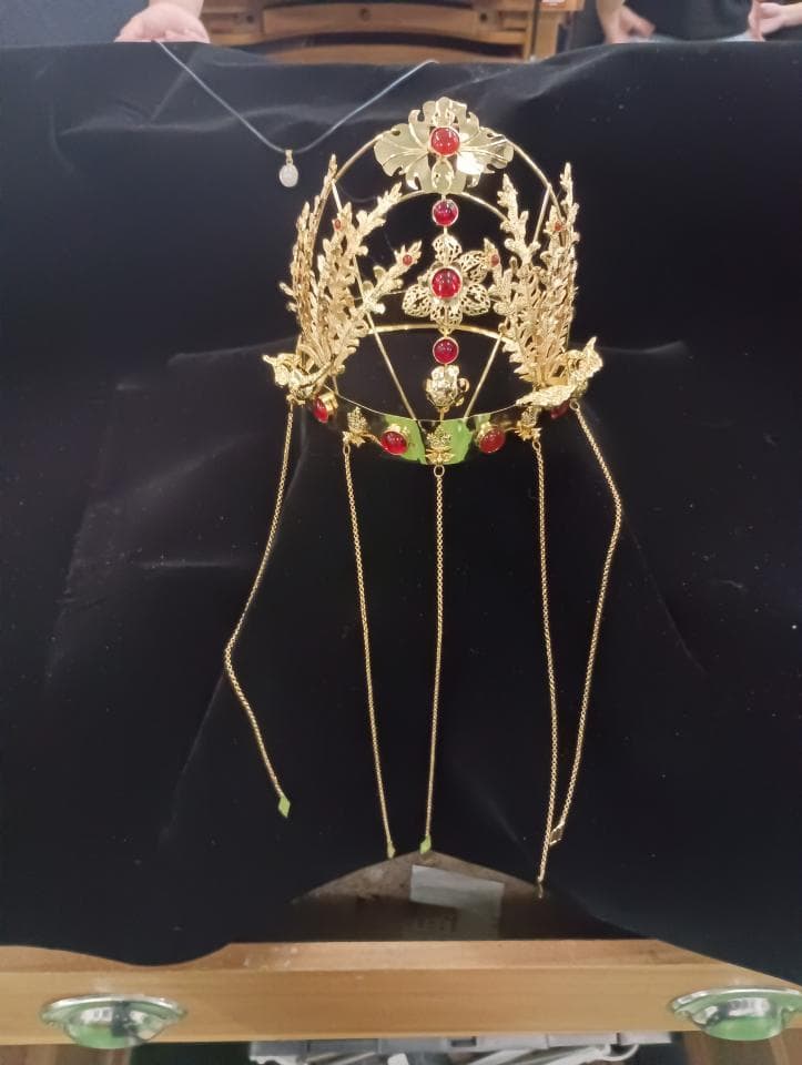 1) 這是一張照片,照片中展示了一個精緻的金色頭飾,頭飾上飾有紅色寶石,頭飾下方有四條金色的鏈子垂下