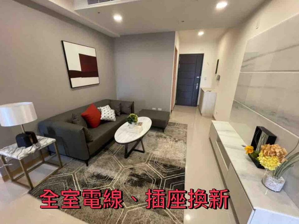 這張照片是一個明亮的客廳,最重要的是一張灰色沙發和一張白色大理石茶几,沙發上擺著紅色的抱枕,茶几上放著盆栽。