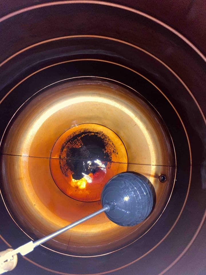 1) 照片顯示一個圓形容器內部的底部,容器的表面有明顯的環狀層,容器底部有黑色的污垢,中央有淺色的污垢,並且有一個灰色圓形工具位於底部