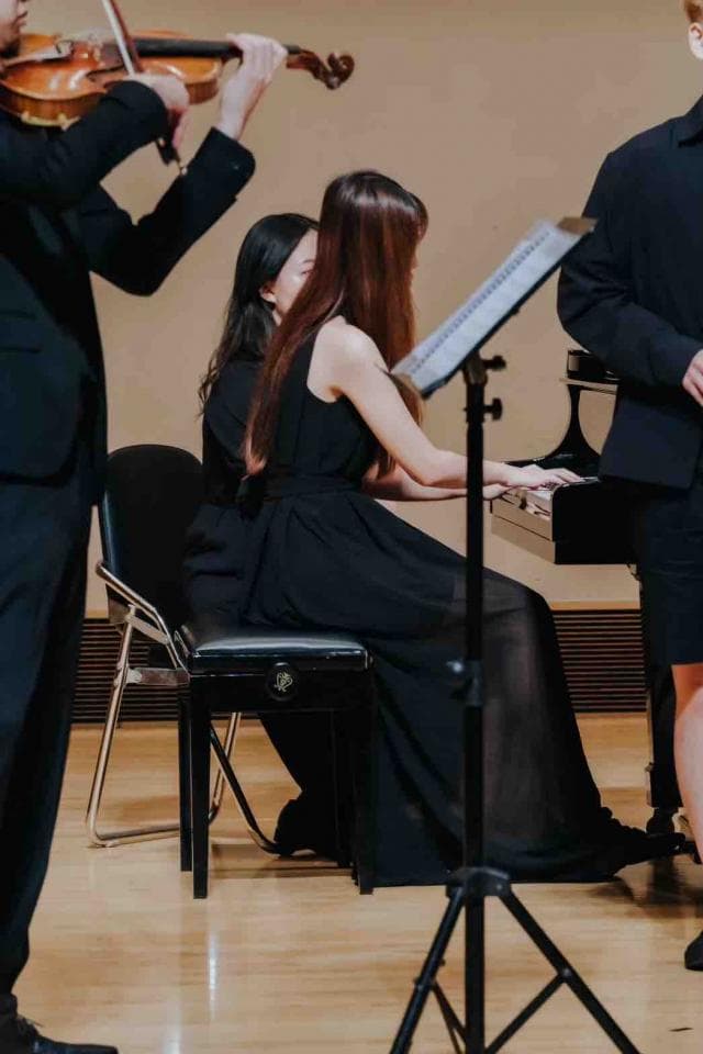 這張「音樂表演」的照片是,一位穿著黑色禮服的女士正在彈鋼琴,一位男士正在演奏小提琴。