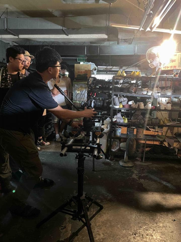 1) 照片顯示一群人在一個倉庫或工作室裡,其中一個人手持攝影機,正在拍攝
