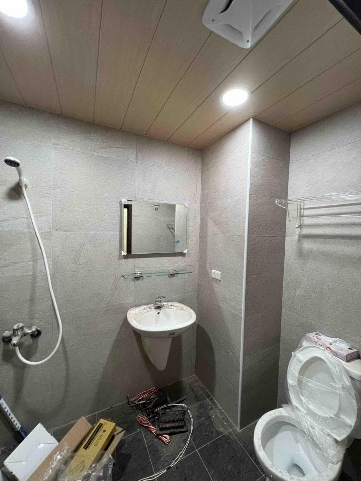 1) 照片顯示一個浴室,裡面有洗手台、馬桶、淋浴頭、鏡子、燈光和一個架子