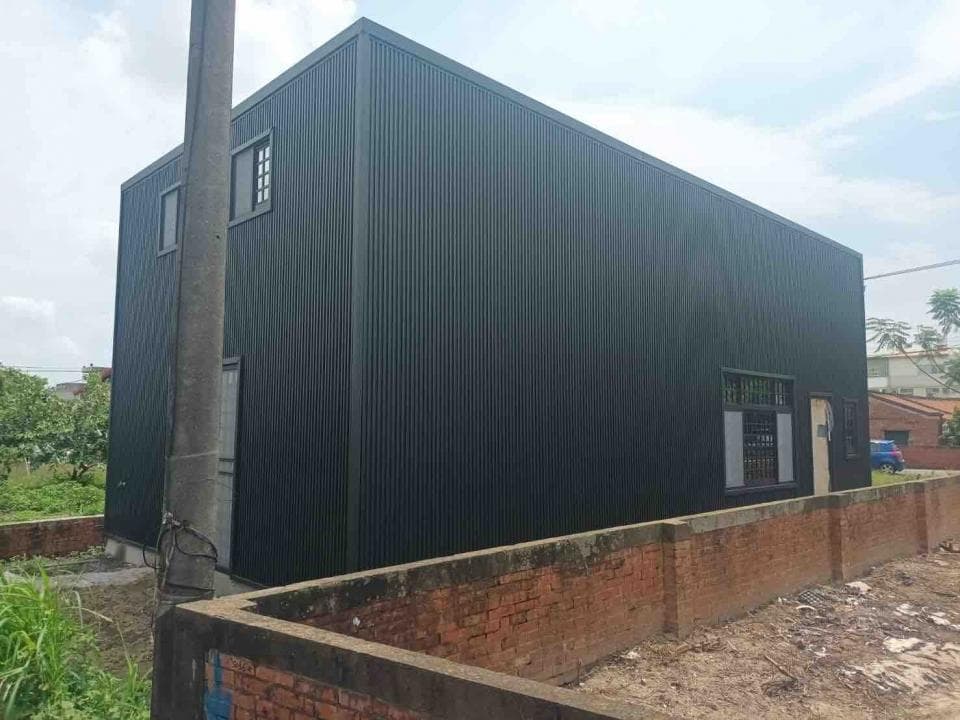 1) 照片顯示一座黑色的金屬屋, 屋頂是斜的, 外牆是金屬波浪板, 屋子外圍有一堵紅磚牆,
2) 建築
3) 住宅
4) 黑色金屬屋,金屬波浪板, 斜屋頂, 紅磚牆,住宅