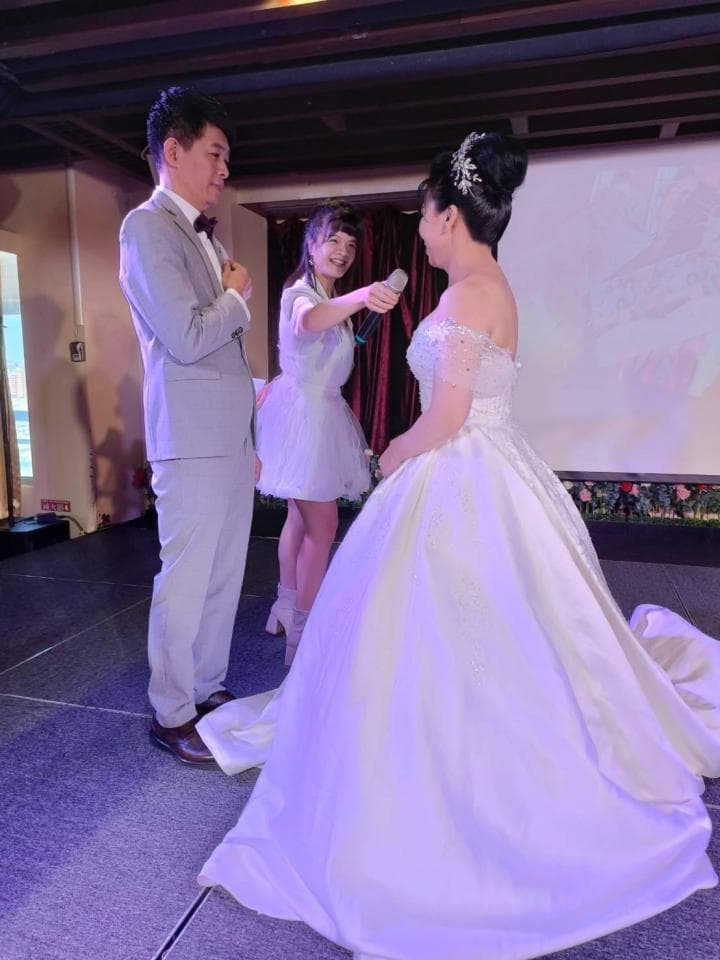 這張照片是一個婚禮現場,最重要的是新娘穿著潔白的婚紗,她手持麥克風,正準備跟賓客說話。