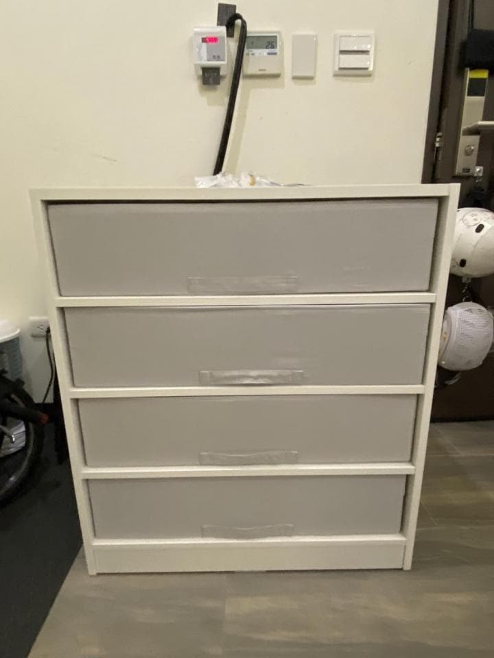 這張照片是一張白色四抽屜的櫃子,櫃子上有四個抽屜,每個抽屜都有一個把手。