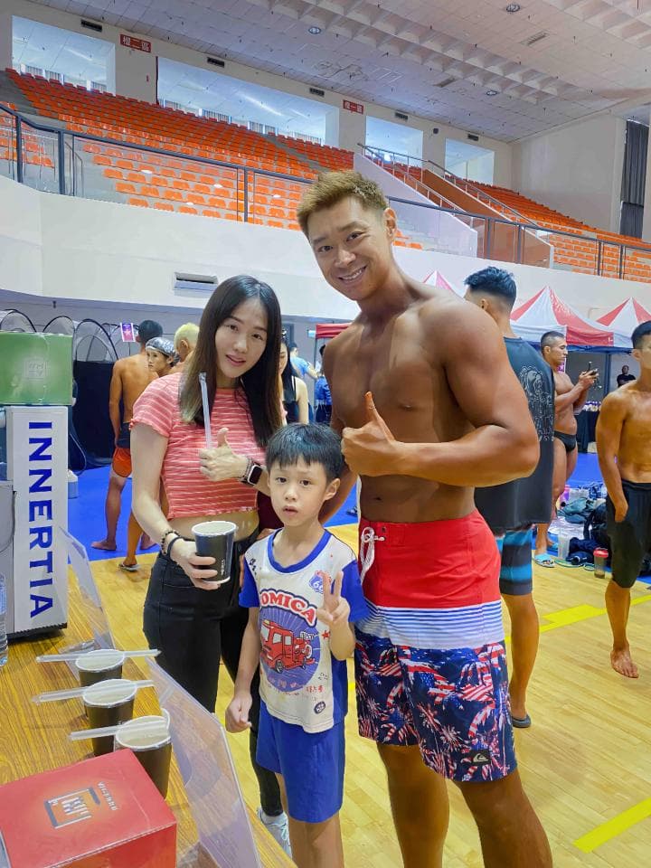 這張照片是三個人在一家飲料店喝飲料。照片裡有一個穿著紅色短褲和藍色短褲的肌肉男,一個穿著紅色條紋短袖和黑色長褲的女生,和一個穿著白色短袖和藍色短褲的男生。他們都面帶笑容,看起來很開心。