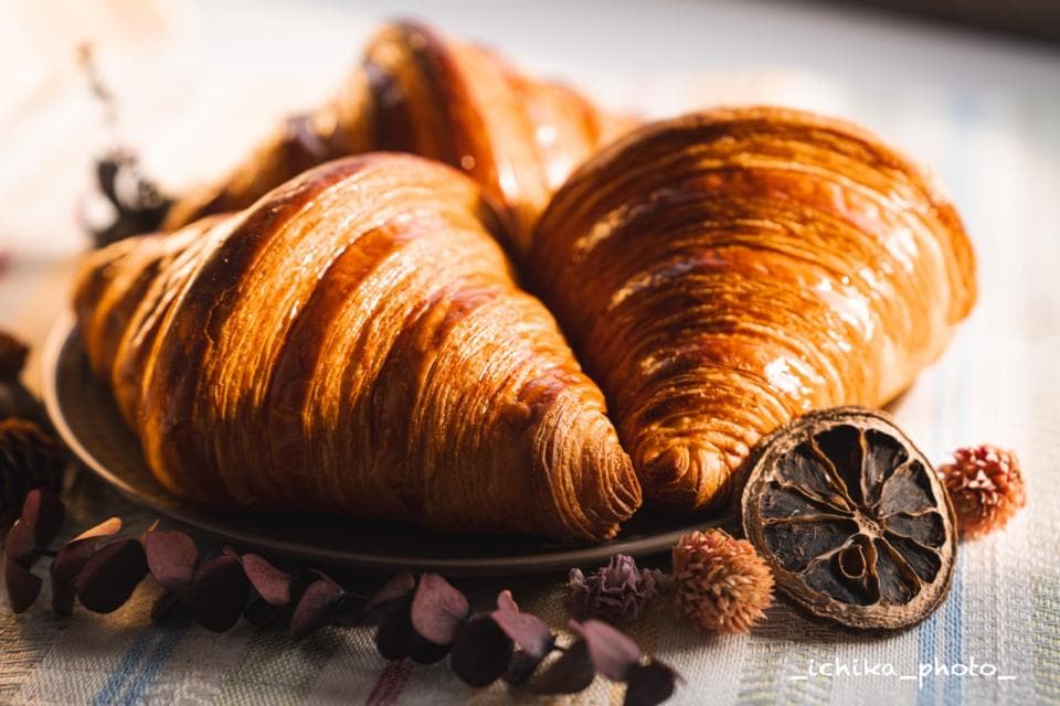 這張「三片可頌」的照片是,三片可頌麵包放在淺色的盤子上,光線照射在上面,呈現金黃色,非常可口。