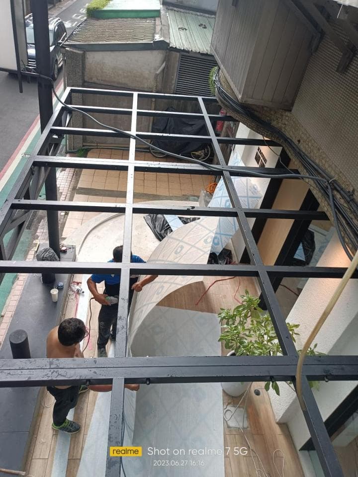 這張照片是一間正在施工的房屋,照片最重要的是房屋頂部的鐵架,鐵架上有工人正在安裝屋頂。