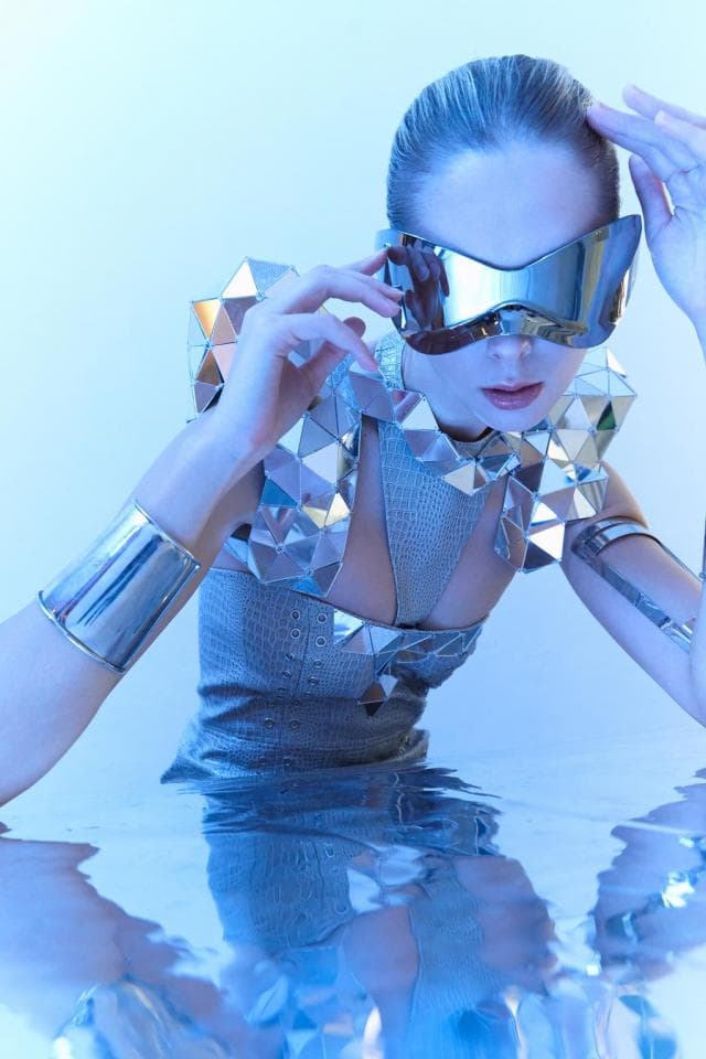 這張照片是一位戴著銀色鏡面眼鏡的女性,她穿著閃閃發光的銀色衣服,並且她的手臂和頭髮看起來像金屬。