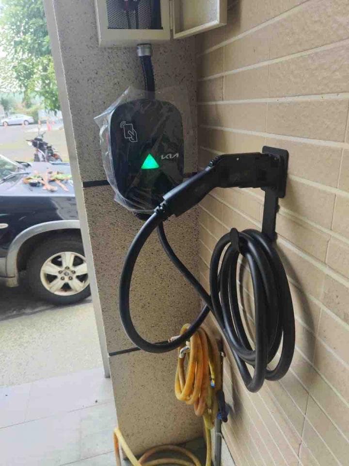 這張照片是一個安裝在牆上的電動車充電器,充電器附帶一個黑色的捲線器和一條黃色的電線。