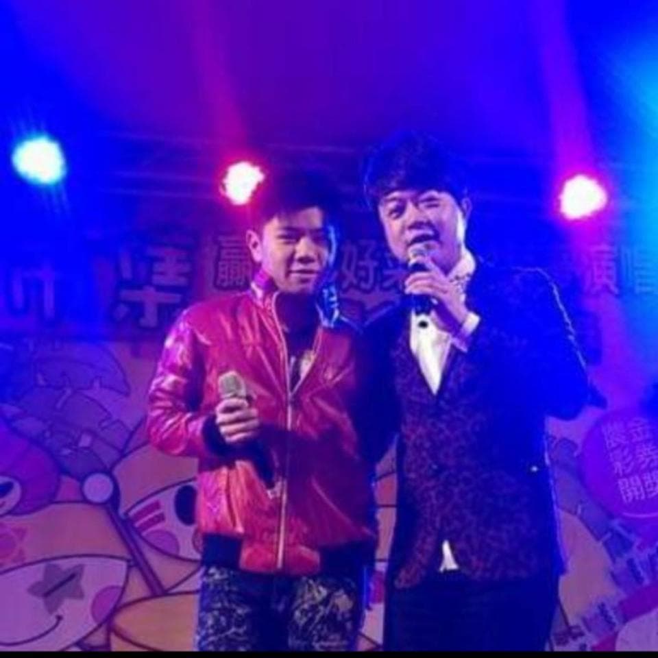 這張照片是兩個男性歌手在舞臺上唱歌,他們都穿著演出服,正在對著麥克風唱歌。左邊的歌手穿著紅色外套,右邊的歌手穿著深色外套,他們都看起來很投入演出。