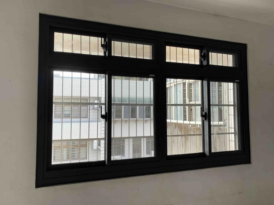 1) 照片顯示一個帶有黑色框架和網格的窗戶,窗戶外是另一個建築物的建築物