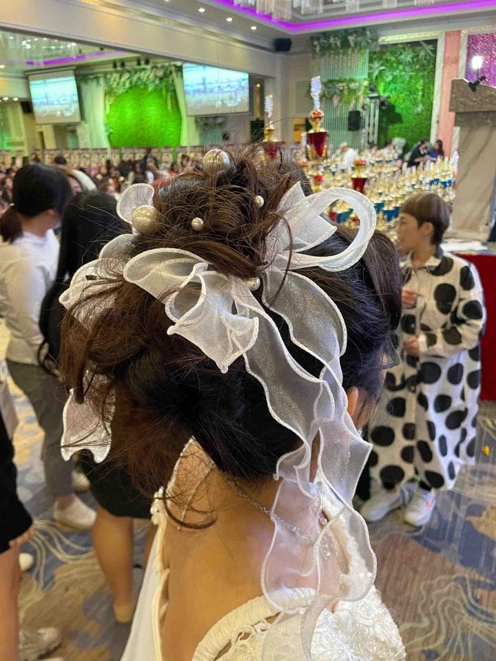 這張照片是一個穿著白色禮服的女性,她頭上戴著一個大的白色緞帶髮飾,髮飾上點綴著一些珍珠。