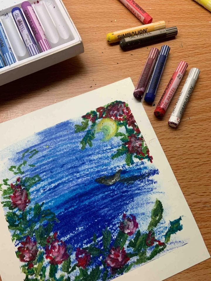 這張照片是一幅用粉蠟筆畫的風景畫,畫中是一片藍色的海,海面上有一輪彎彎的月亮,海邊開滿了紅色的花。