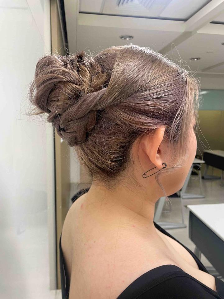 這張「女生背影」的照片是,一個穿著黑色上衣的女生,她的頭髮被盤成一個高高的髮髻,髮髻上有一個髮夾,女生脖子後面有一個別針。