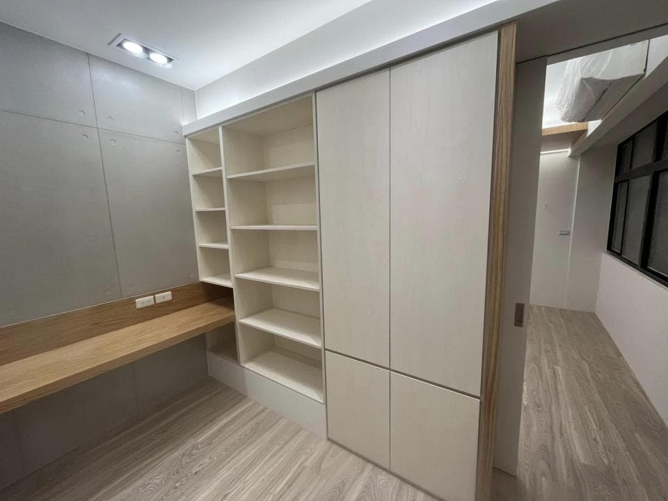 這張照片是一間現代化的臥室,照片最主要的部分是牆上的白色櫃子,它設計精緻,有許多層架可以放書和其他物品,櫃子右側有一個滑門,門後可能是一個衣櫃或儲物空間。