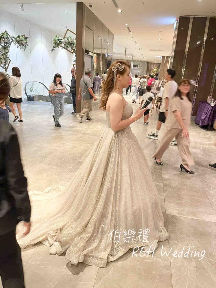 這張照片是一個美麗的新娘,她穿著閃閃發光的婚紗,手持麥克風,站在一個裝飾華麗的宴會廳中。她看起來非常幸福,準備好享受她特殊的日子。